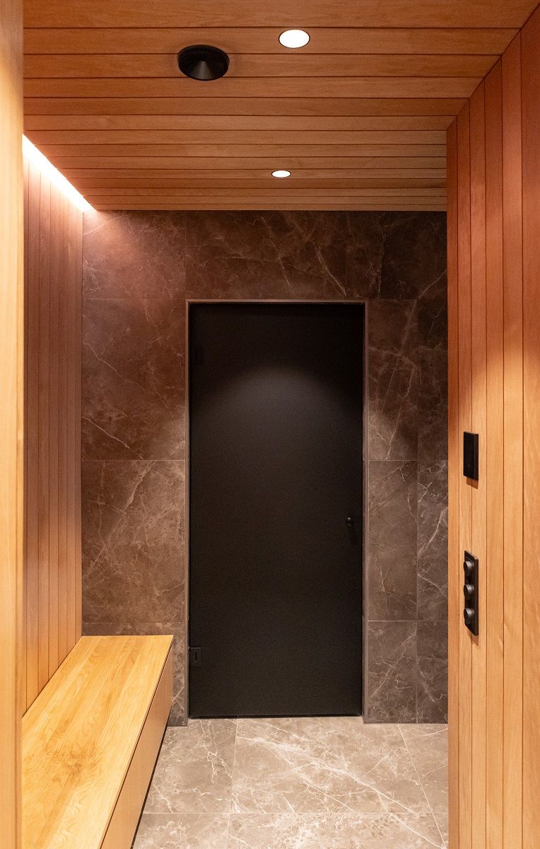 Nel corridoio degli spogliatoi, faretti LED a incasso nel soffitto e illuminazione indiretta a strisce LED sopra la panca al limite del soffitto.